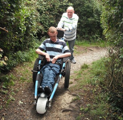 Hippocampe all-terrain wheelchair being pushed along a woodland path